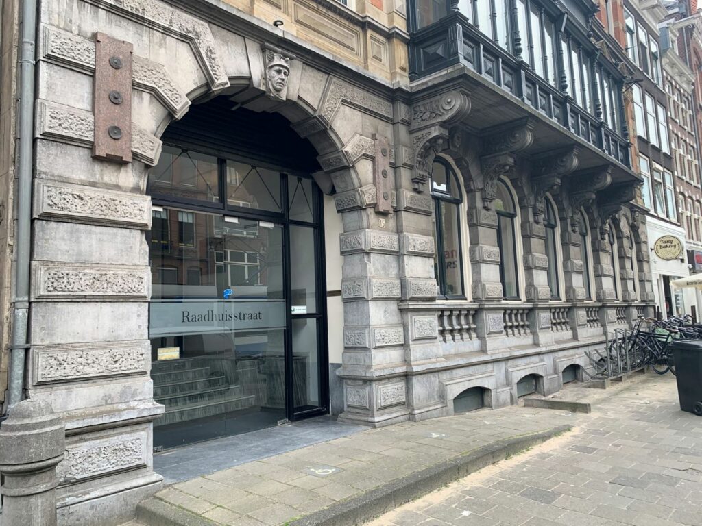 Ingang van een historisch gebouw aan de Raadhuisstraat met sierlijke gevel en gegraveerde naam op het glas.