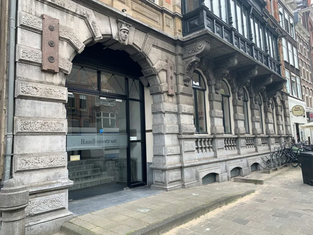 Ingang van een historisch gebouw aan de Raadhuisstraat met sierlijke gevel en gegraveerde naam op het glas.