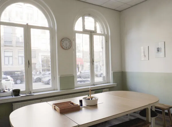 Lichte vergaderruimte aan de Raadhuisstraat met grote ronde ramen, een houten tafel en uitzicht op de straat.