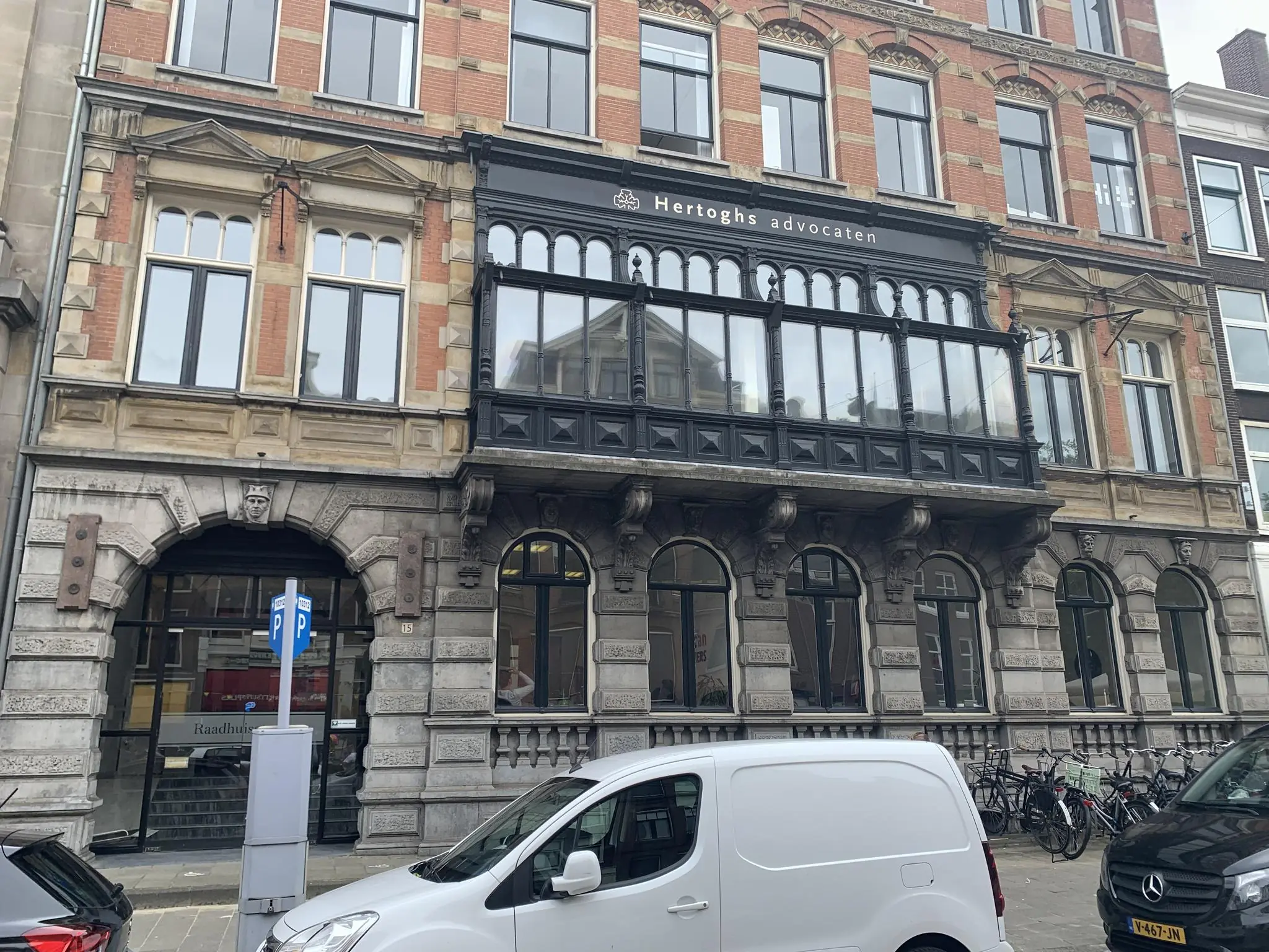 Voorgevel van het historische kantoorpand van Hertoghs advocaten aan de Raadhuisstraat, met geparkeerde auto's en fietsen op de voorgrond.