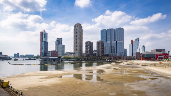 Skyline van Rotterdam met zicht op de Rijnhavenkade, hoogbouw en het zandige bouwterrein op de voorgrond.