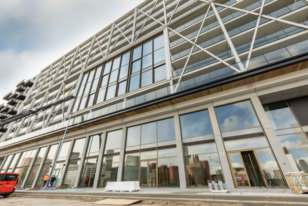 Moderne gevel van een nieuwbouwcomplex aan de Rijnhavenkade met grote glazen ramen en zicht op de skyline van Rotterdam.