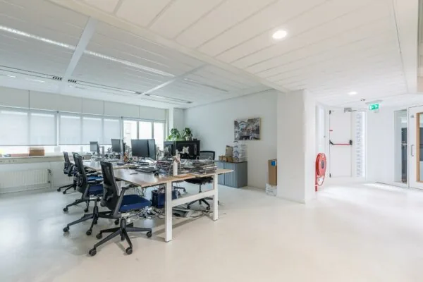 Modern kantoor aan het Leidseveer met meerdere werkplekken, bureaustoelen en computerschermen in een lichte ruimte.