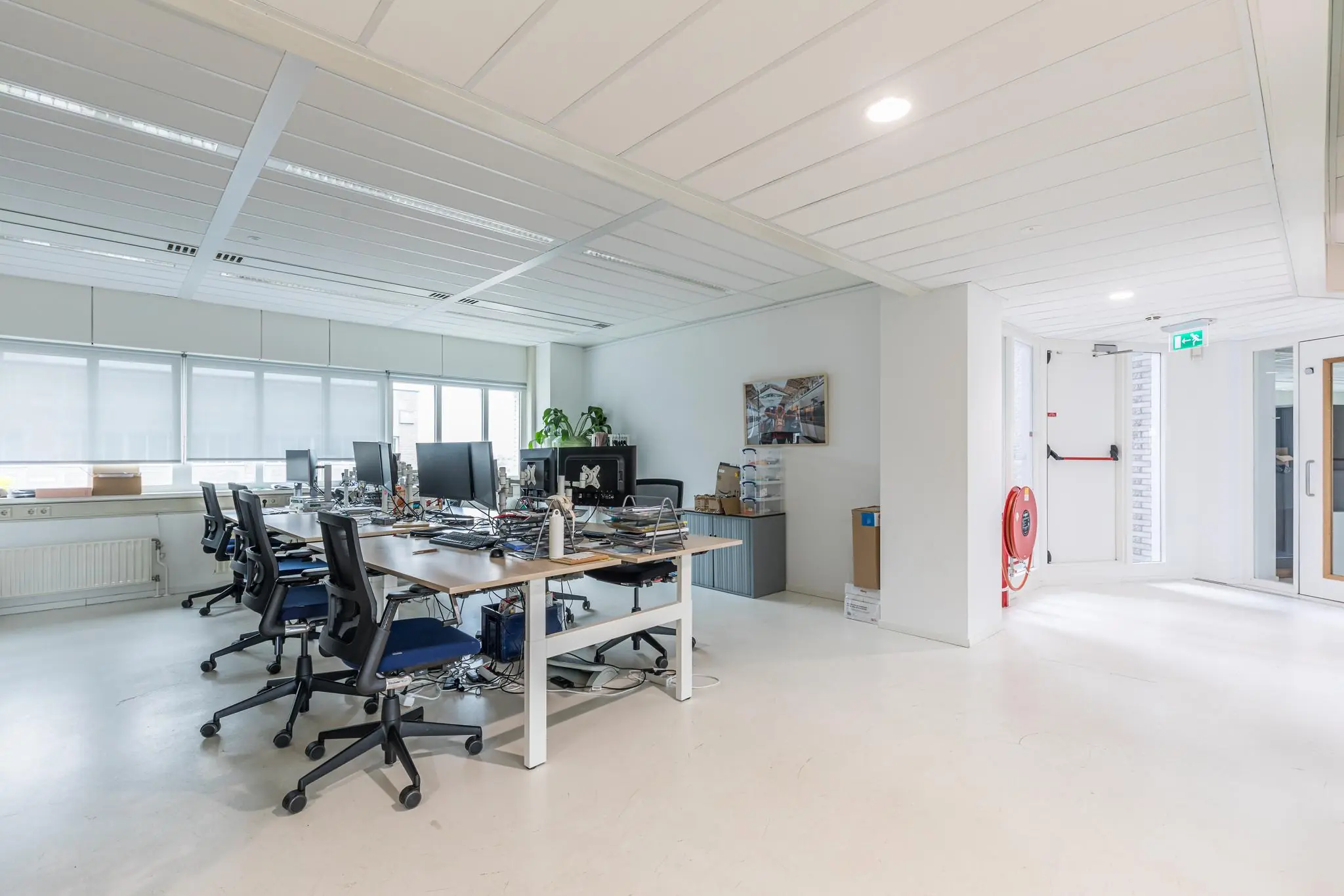 Modern kantoor aan het Leidseveer met meerdere werkplekken, bureaustoelen en computerschermen in een lichte ruimte.
