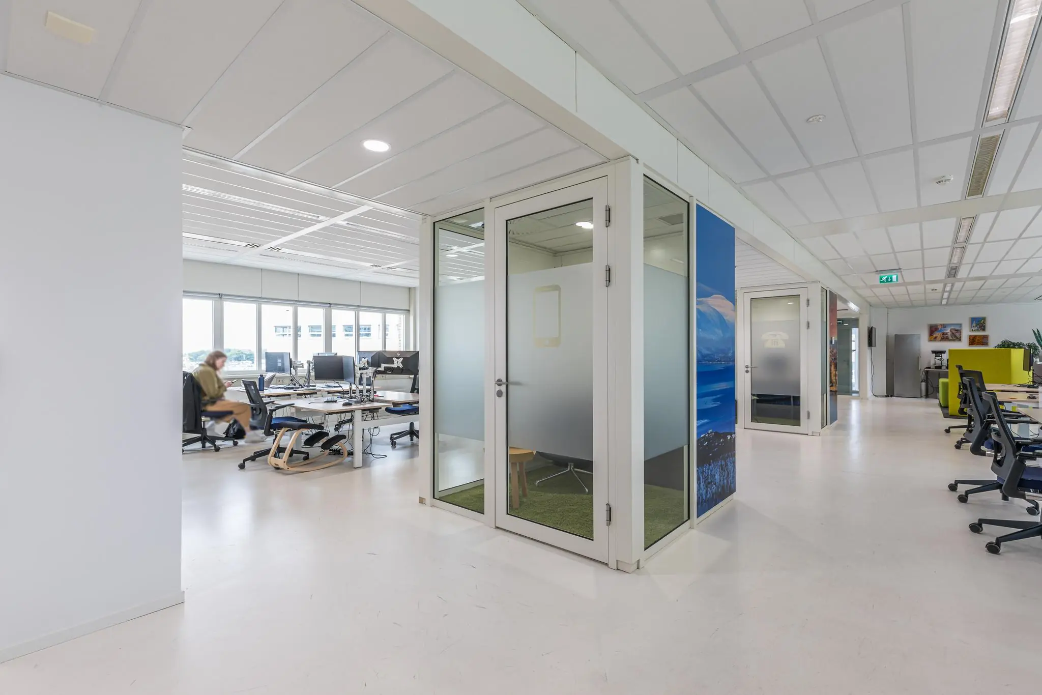 Moderne open kantoorruimte aan het Leidseveer met glazen belcellen en werkplekken bij grote ramen.