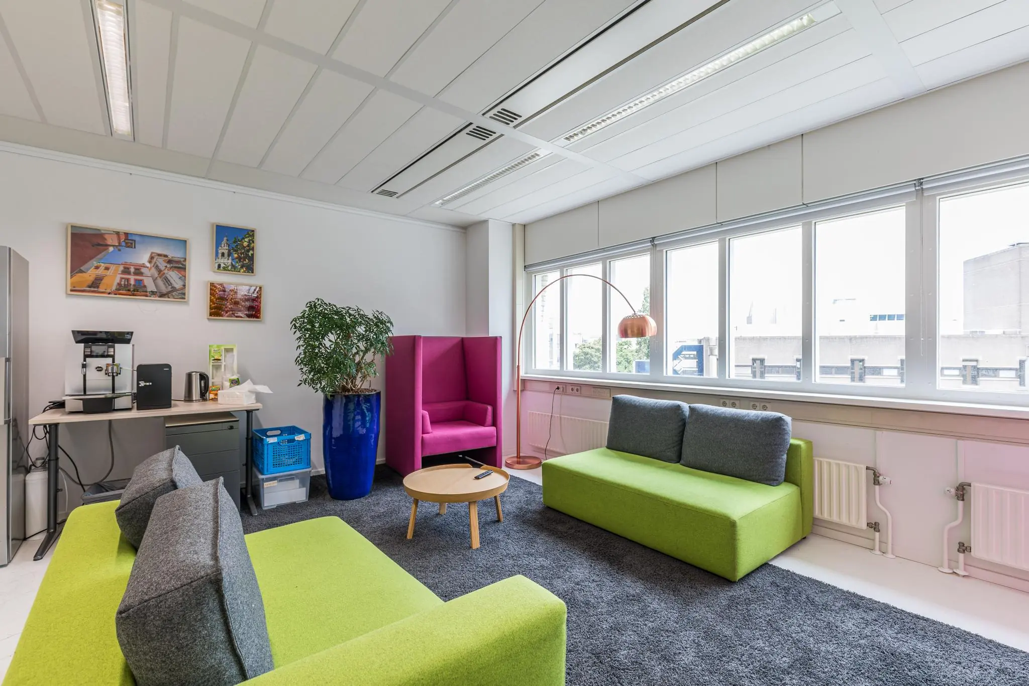 Moderne loungehoek in een kantoor aan het Leidseveer, ingericht met felgekleurde meubels, een koffiecorner en grote ramen met uitzicht op de stad.