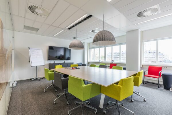 Vergaderruimte Leidseveer met moderne inrichting, kleurrijke stoelen, groot scherm en flip-over.