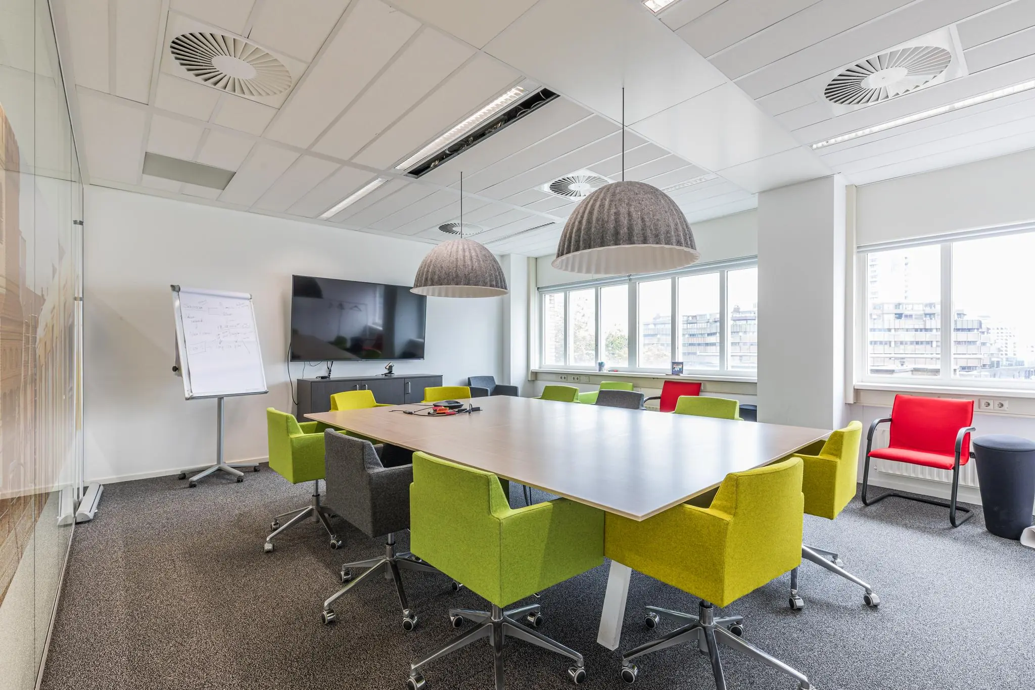 Vergaderruimte Leidseveer met moderne inrichting, kleurrijke stoelen, groot scherm en flip-over.
