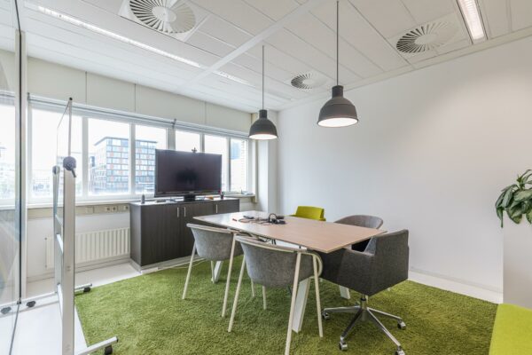 Moderne vergaderruimte in kantoorgebouw Leidseveer met grote ramen, groen vloerkleed en een flatscreen op kast.