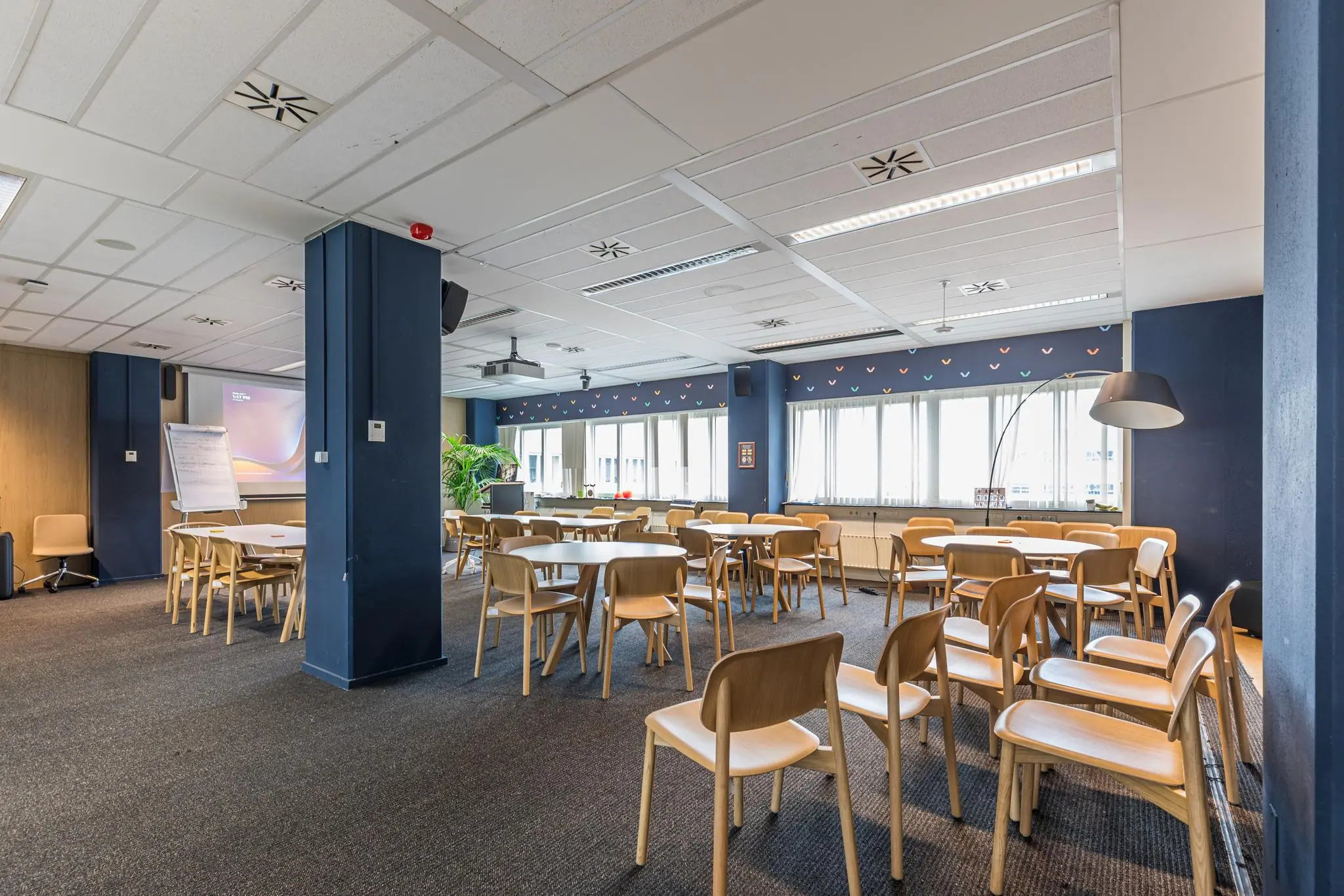 Ruime vergaderruimte aan het Leidseveer met houten stoelen, ronde tafels, een projector en veel daglicht.