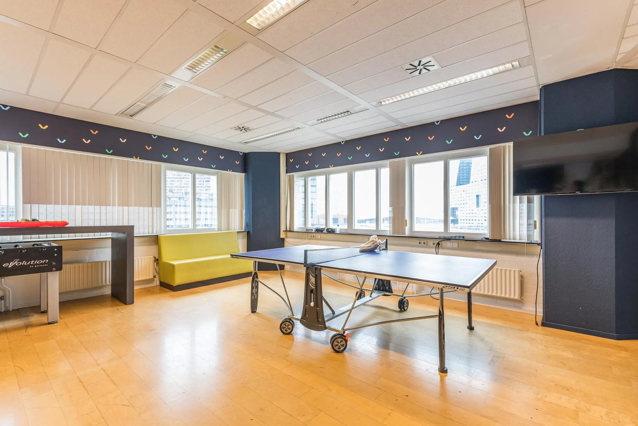 Licht recreatieruimte in kantoorpand aan het Leidseveer met een tafeltennistafel, zitbank en uitzicht op de stad.