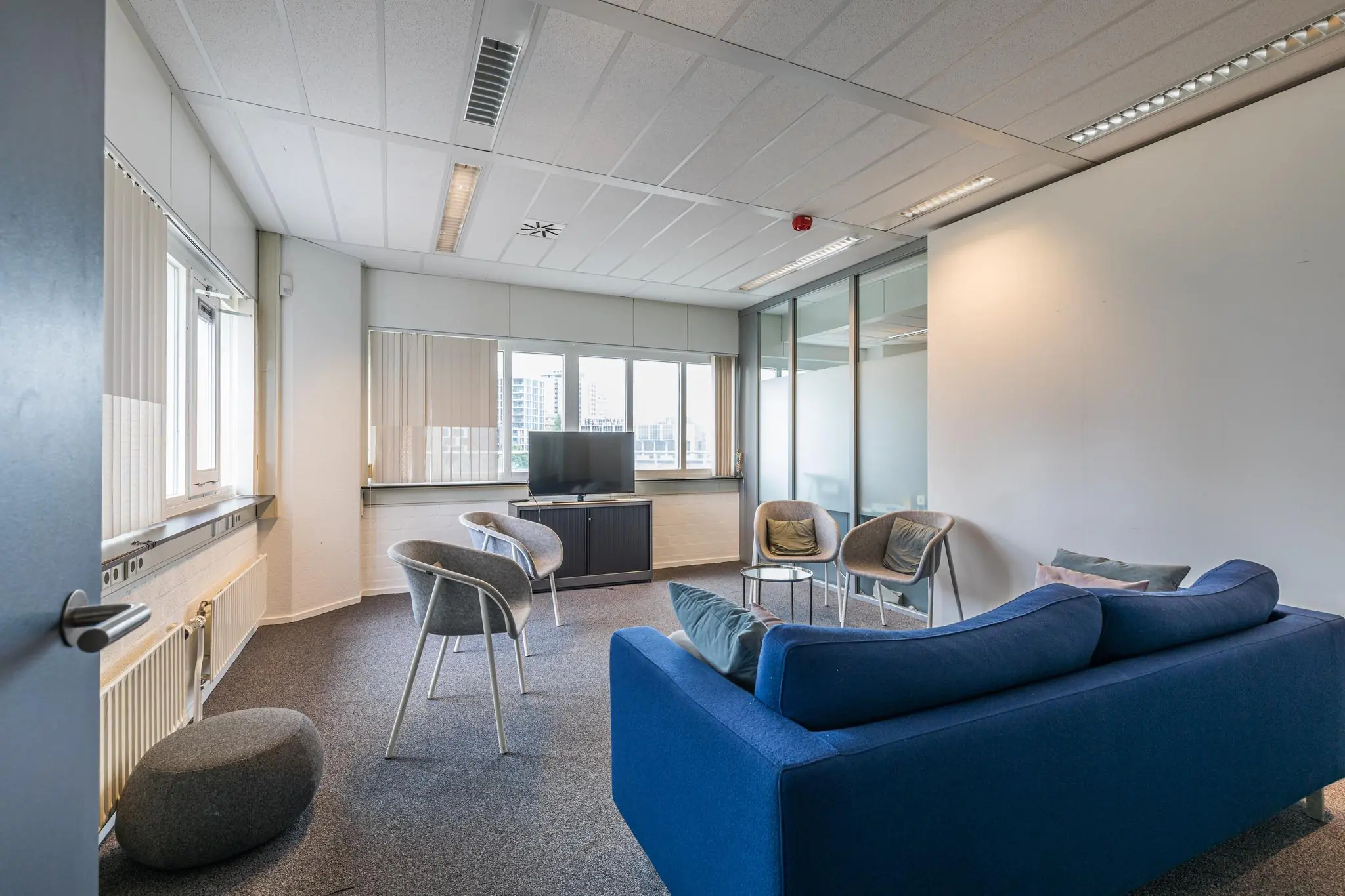Moderne wachtruimte of lounge in kantoorpand Leidseveer met zitplaatsen, flatscreen-tv en grote ramen.