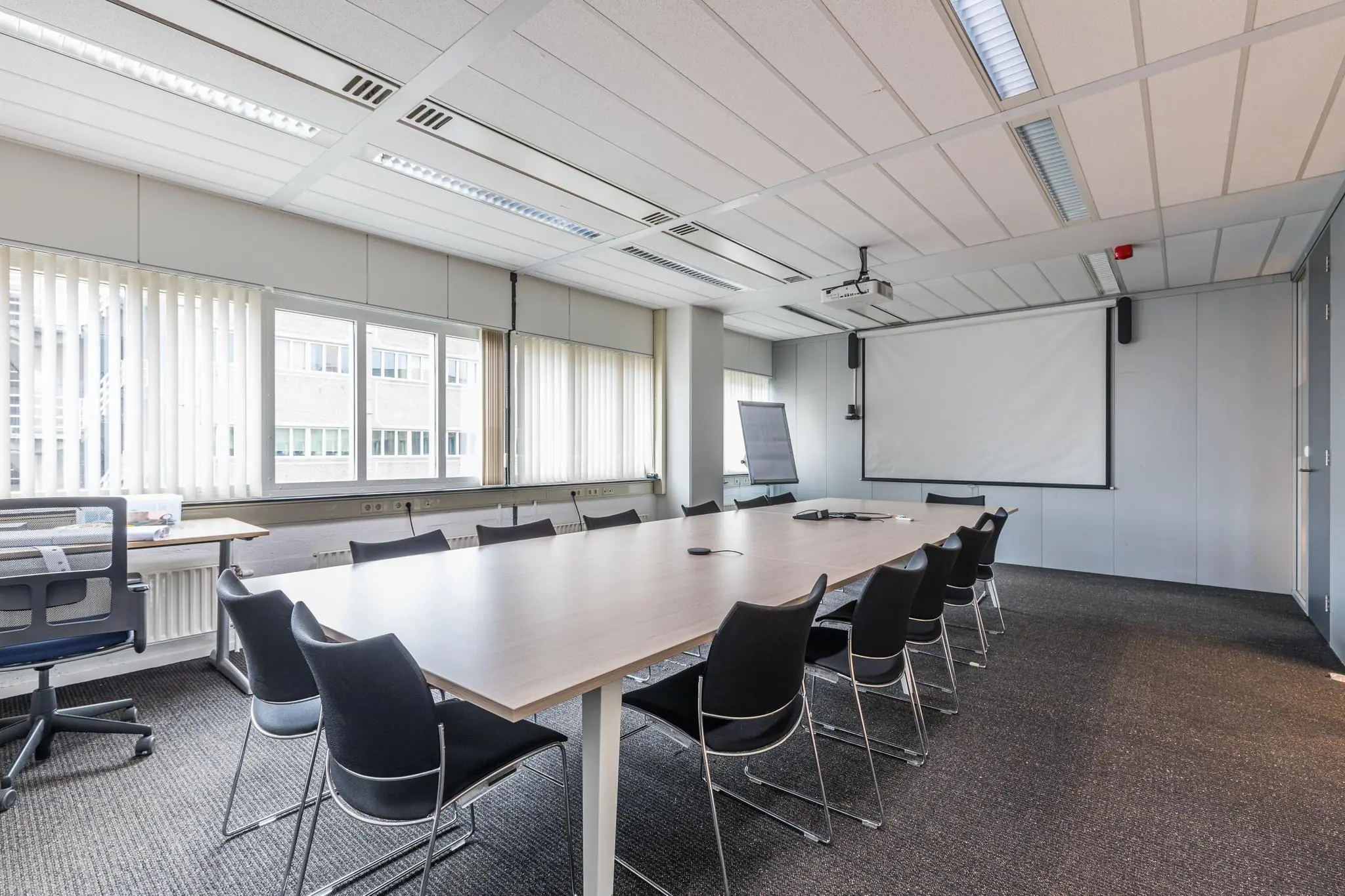 Vergaderruimte in kantoorpand aan het Leidseveer met lange tafel, stoelen, projectiescherm en flip-over.