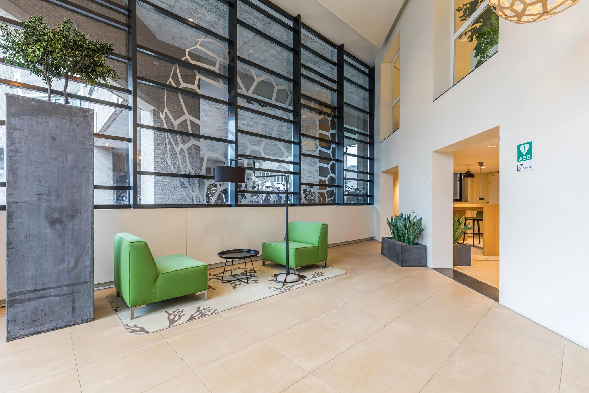 Moderne wachtruimte in het Leidseveer met groene stoelen, hoge ramen en planten.