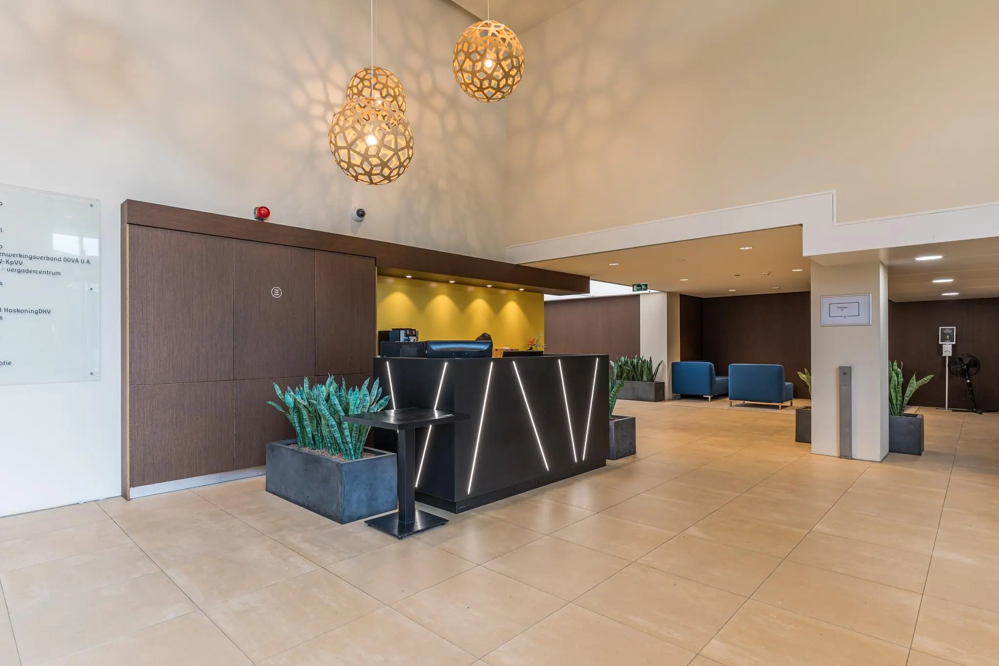 Moderne ontvangsthal van Leidseveer met een strakke balie, stijlvolle hanglampen en zitgedeelte met blauwe stoelen.