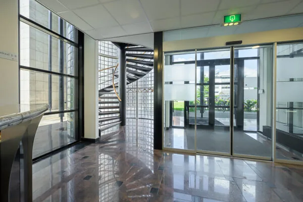 Ingang van een modern kantoor aan de Rivium Westlaan met glazen deuren, een wenteltrap en marmeren vloer.