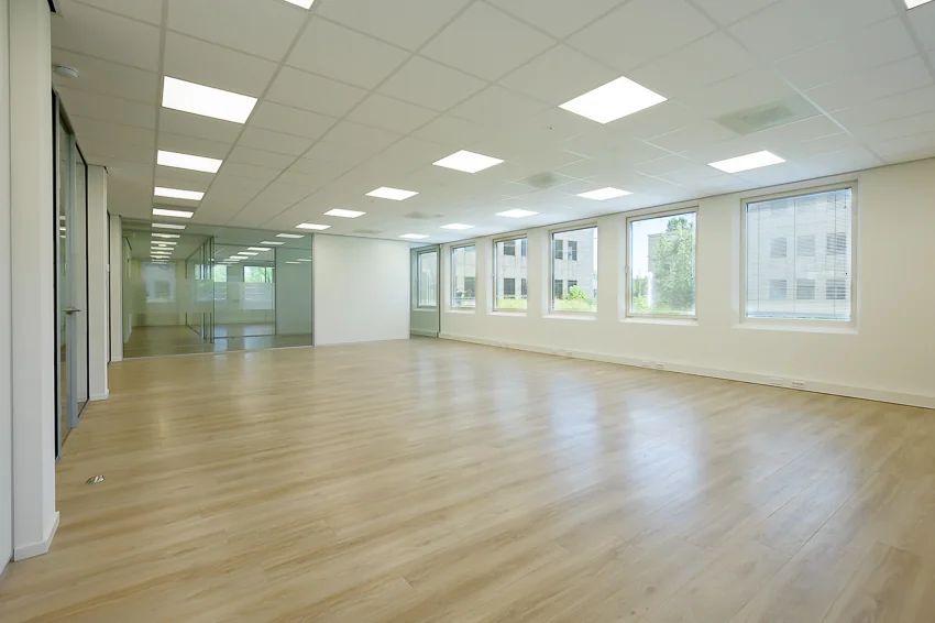 Lichte, lege kantoorruimte aan de Rivium Westlaan met houten vloer, systeemplafond en glazen wanden.