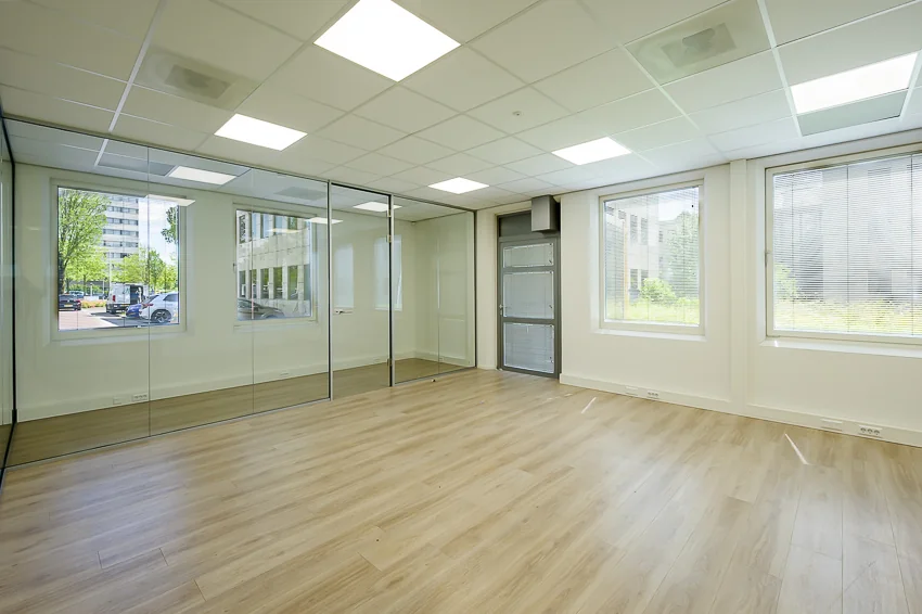 Lichte, lege kantoorruimte aan de Rivium Westlaan met glazen scheidingswand en houten vloer.