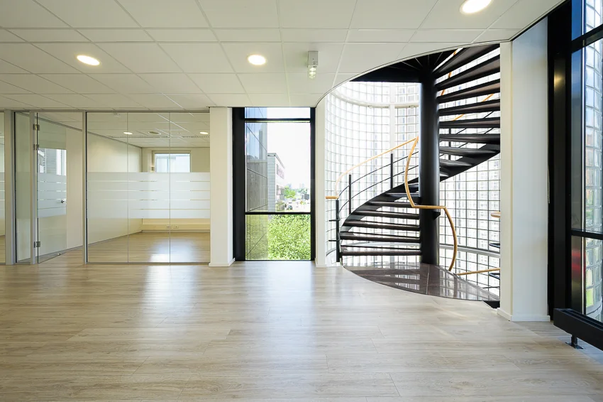 Moderne kantoorruimte aan de Rivium Westlaan met glazen wanden en een zwarte wenteltrap bij een grote raampartij.