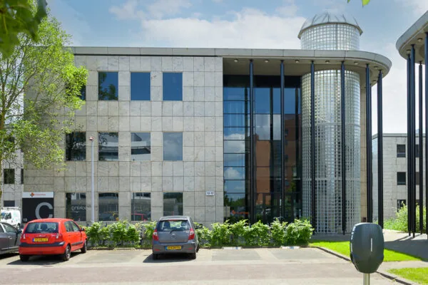 Kantoorgebouw aan de Rivium Westlaan met een glazen entree en ronde toren, gezien vanaf de parkeerplaats.