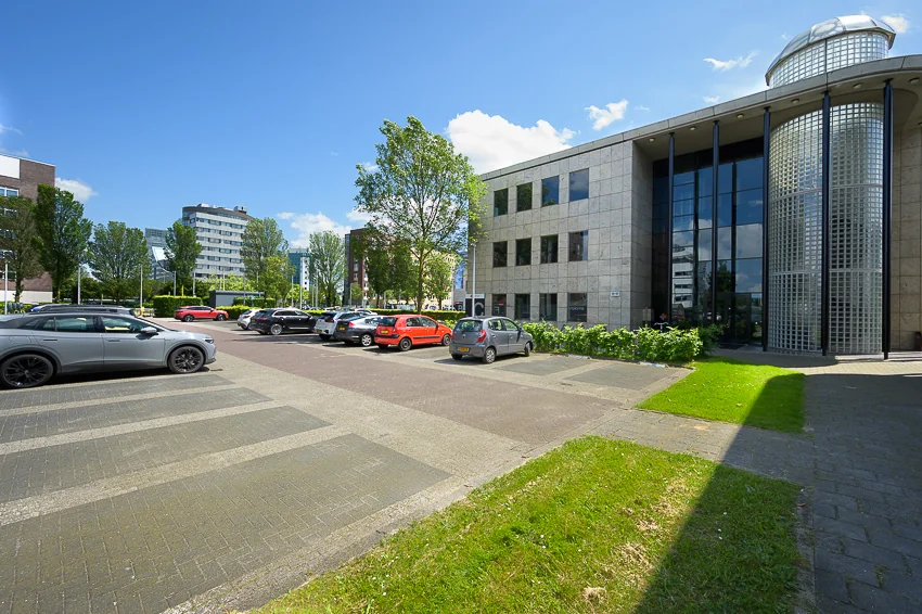 Kantoorgebouw aan de Rivium Westlaan met parkeerplaats en geparkeerde auto's op een zonnige dag.