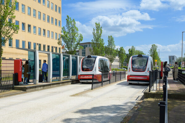 Twee zelfrijdende ParkShuttle-voertuigen bij een halte aan de Rivium Westlaan in Capelle aan den IJssel.
