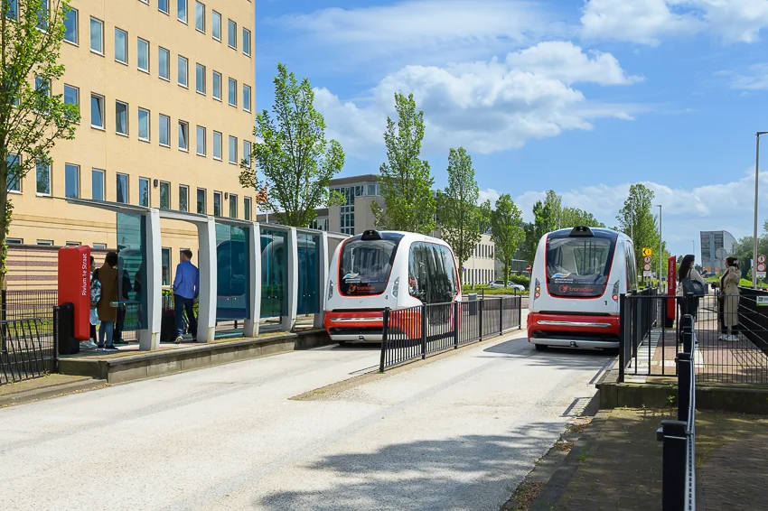 Twee zelfrijdende ParkShuttle-voertuigen bij een halte aan de Rivium Westlaan in Capelle aan den IJssel.