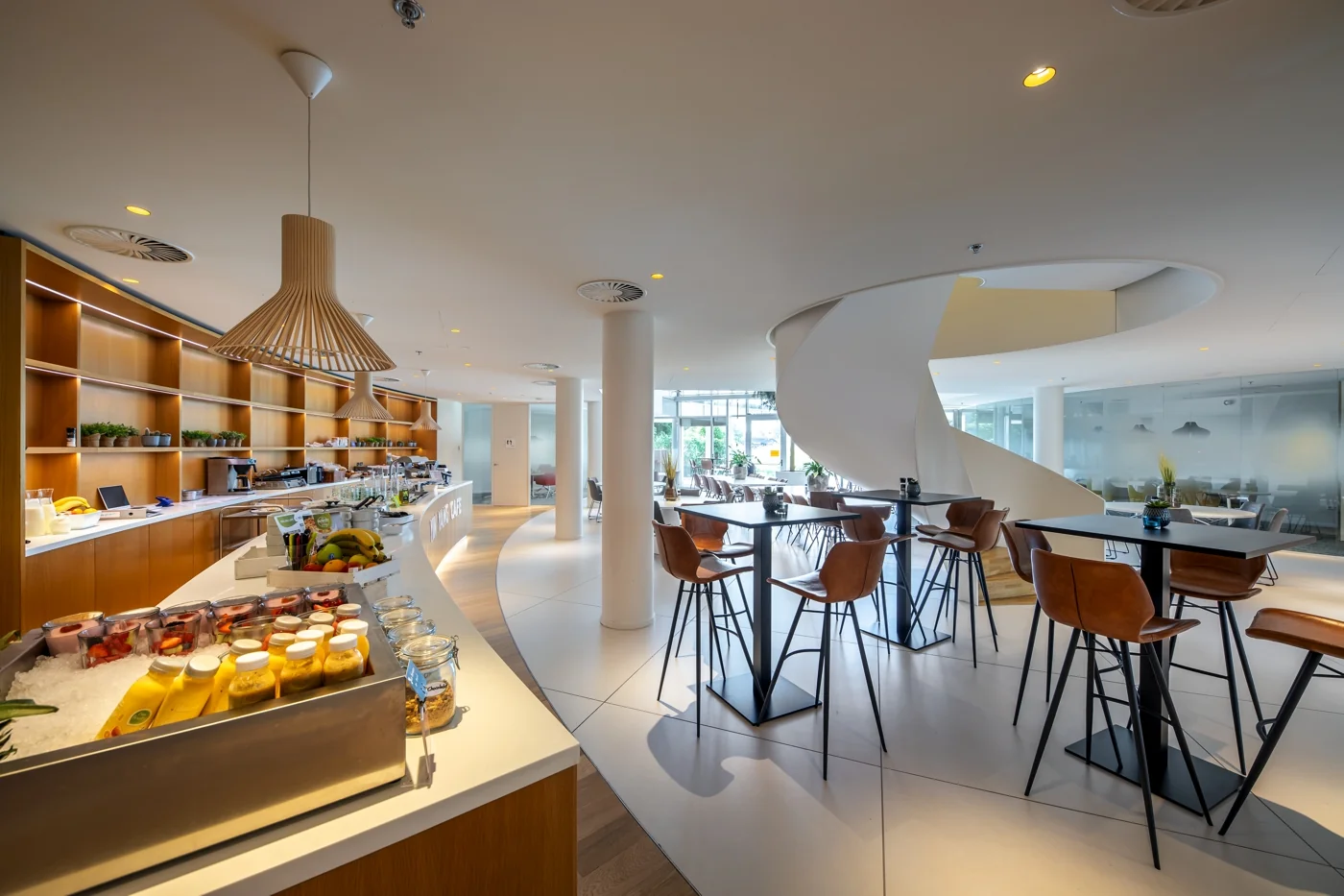 Moderne en lichte bedrijfsrestaurant aan de Euclideslaan met hoge tafels, een buffet en een opvallende witte wenteltrap.