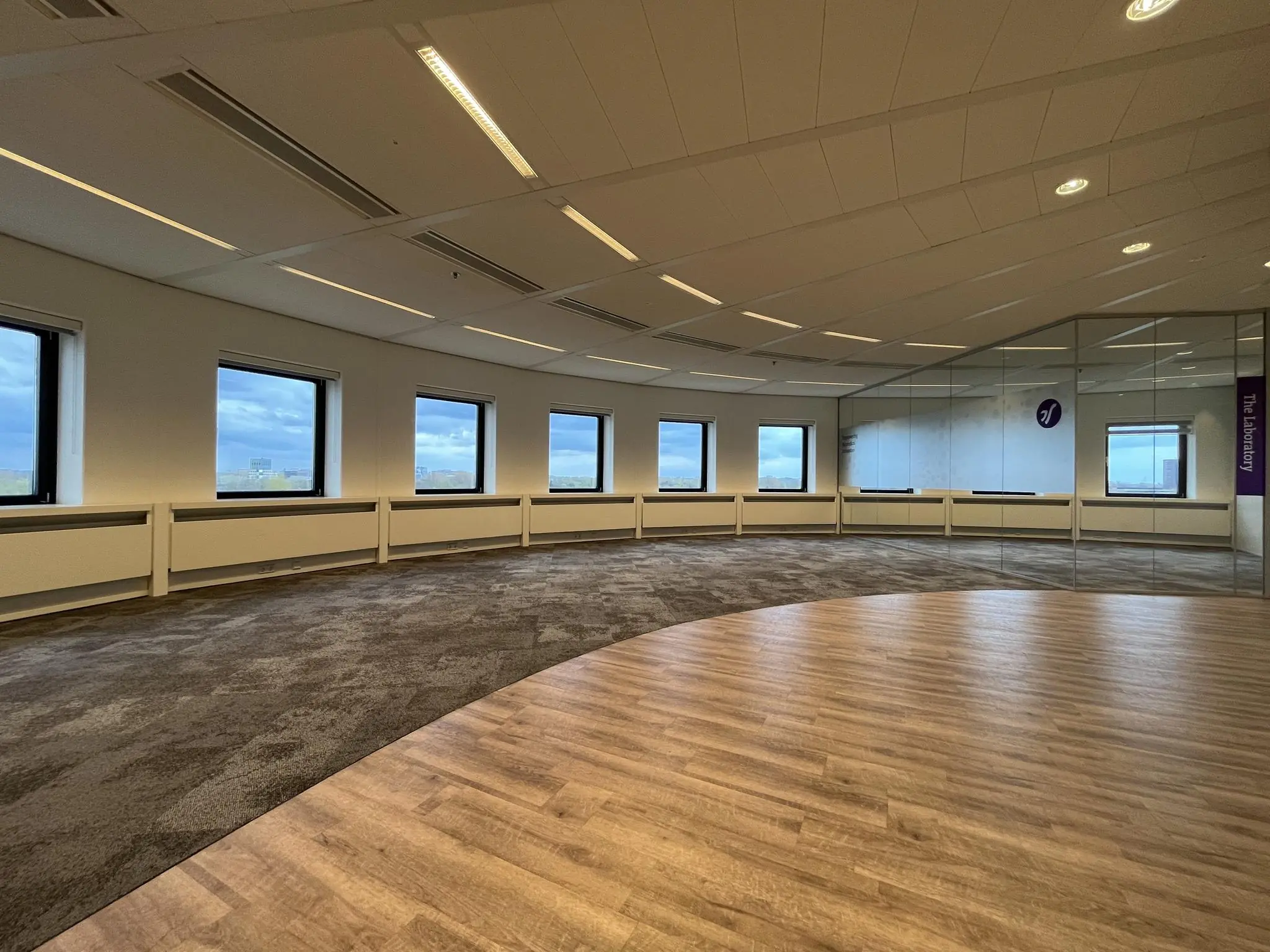 Moderne, lege kantoorruimte aan de Euclideslaan met grote ramen, glazen wand en gedeeltelijk tapijt- en houtenvloer.