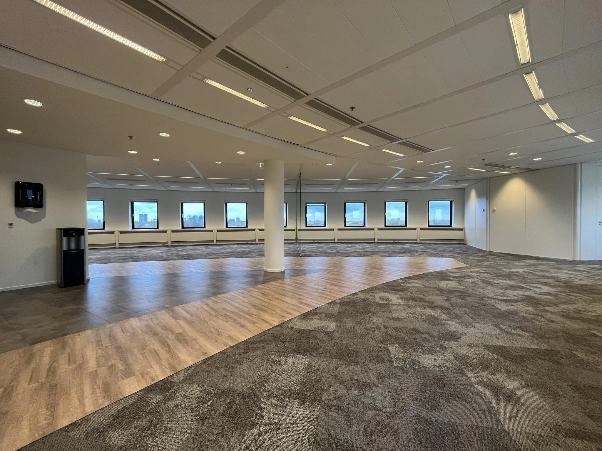 Ruime, lege kantoorruimte aan de Euclideslaan met tapijt, houten vloeraccenten en een rij ramen met uitzicht op de stad.