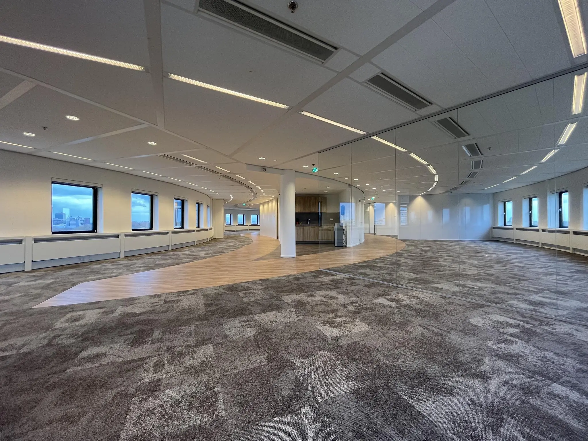 Moderne, lege kantoorruimte aan de Euclideslaan met gebogen ramen en een opvallend vloerpatroon van tapijt en hout.