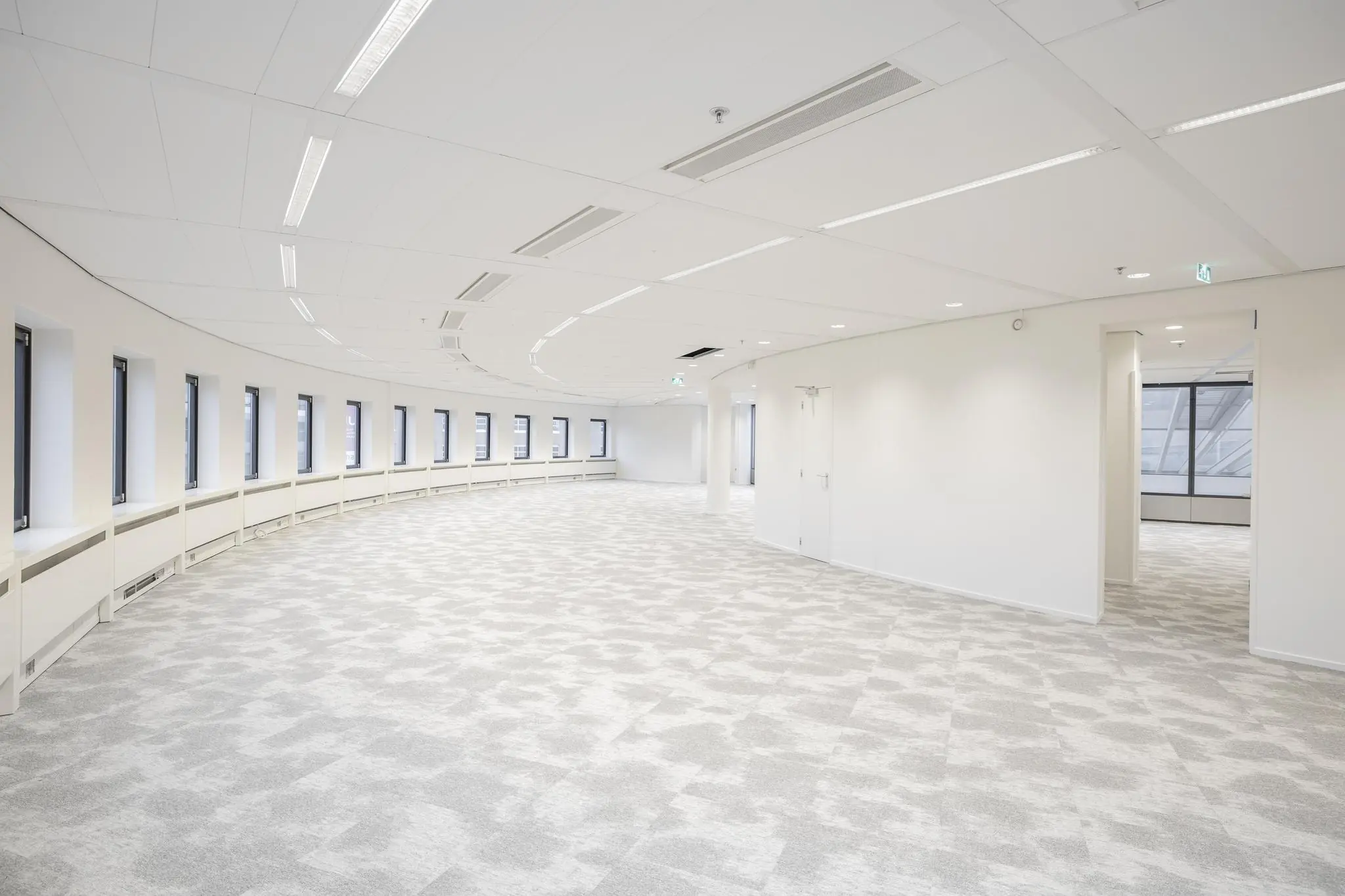 Licht, modern en leeg kantoorinterieur aan de Euclideslaan met gebogen raamwand en grijs tapijt.