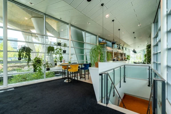 Een moderne kantoorruimte met veel planten, een glazen wand en een trap die naar beneden leidt.