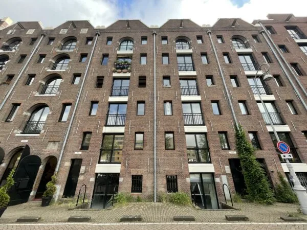 Vooraanzicht van een voormalig pakhuis aan het Entrepotdok in Amsterdam met bakstenen gevel en industriële raampartijen.