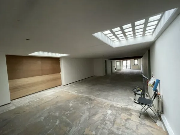 Leegstaand appartement aan het Entrepotdok met een betonnen vloer, witte muren en grote lichtkoepels in het plafond.