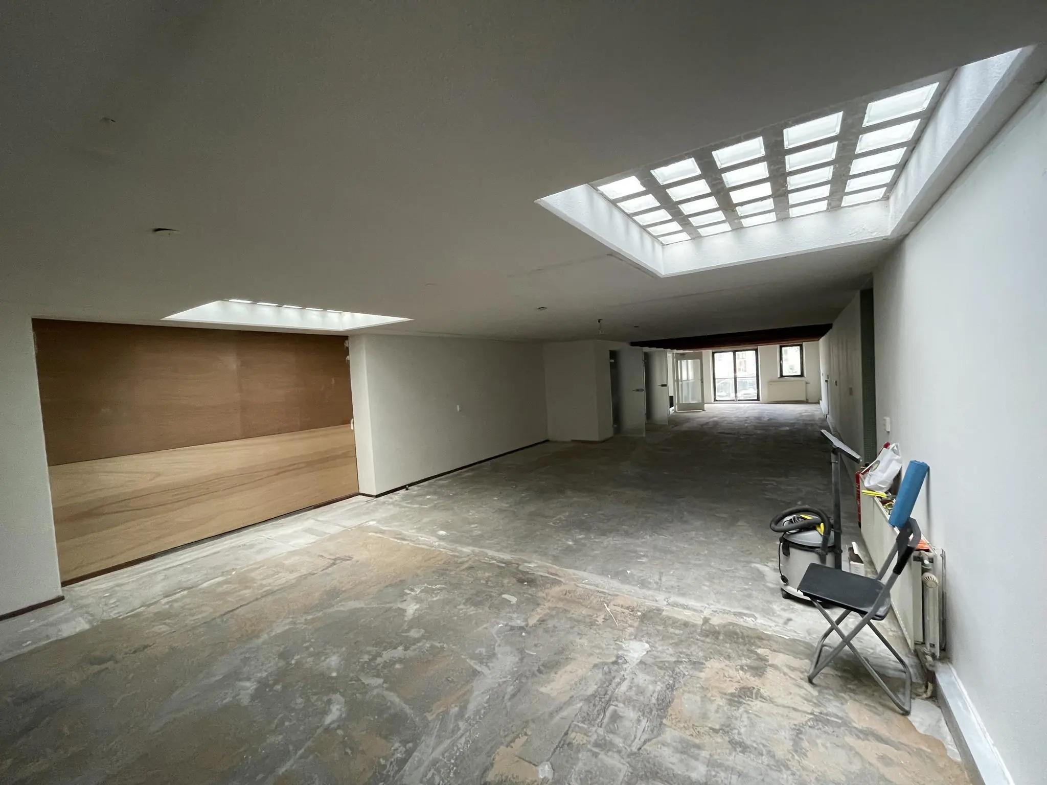 Leegstaand appartement aan het Entrepotdok met een betonnen vloer, witte muren en grote lichtkoepels in het plafond.