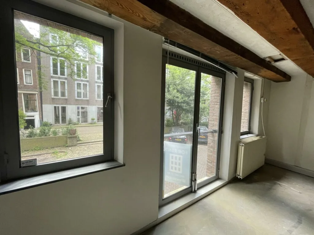 Interieur van een leegstaand pand aan het Entrepotdok met grote ramen en zicht op een rustige straat.