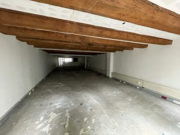 Lege, langgerekte ruimte met betonnen vloer, houten balkenplafond en witte muren in het Entrepotdok.