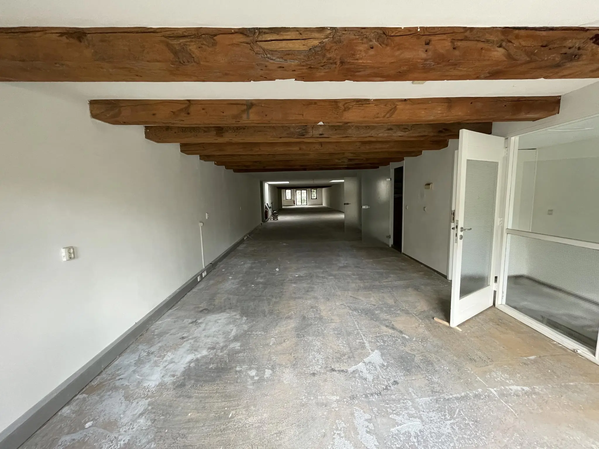 Langwerpige, lege ruimte in het Entrepotdok met zichtbare houten plafondbalken en een betonnen vloer.