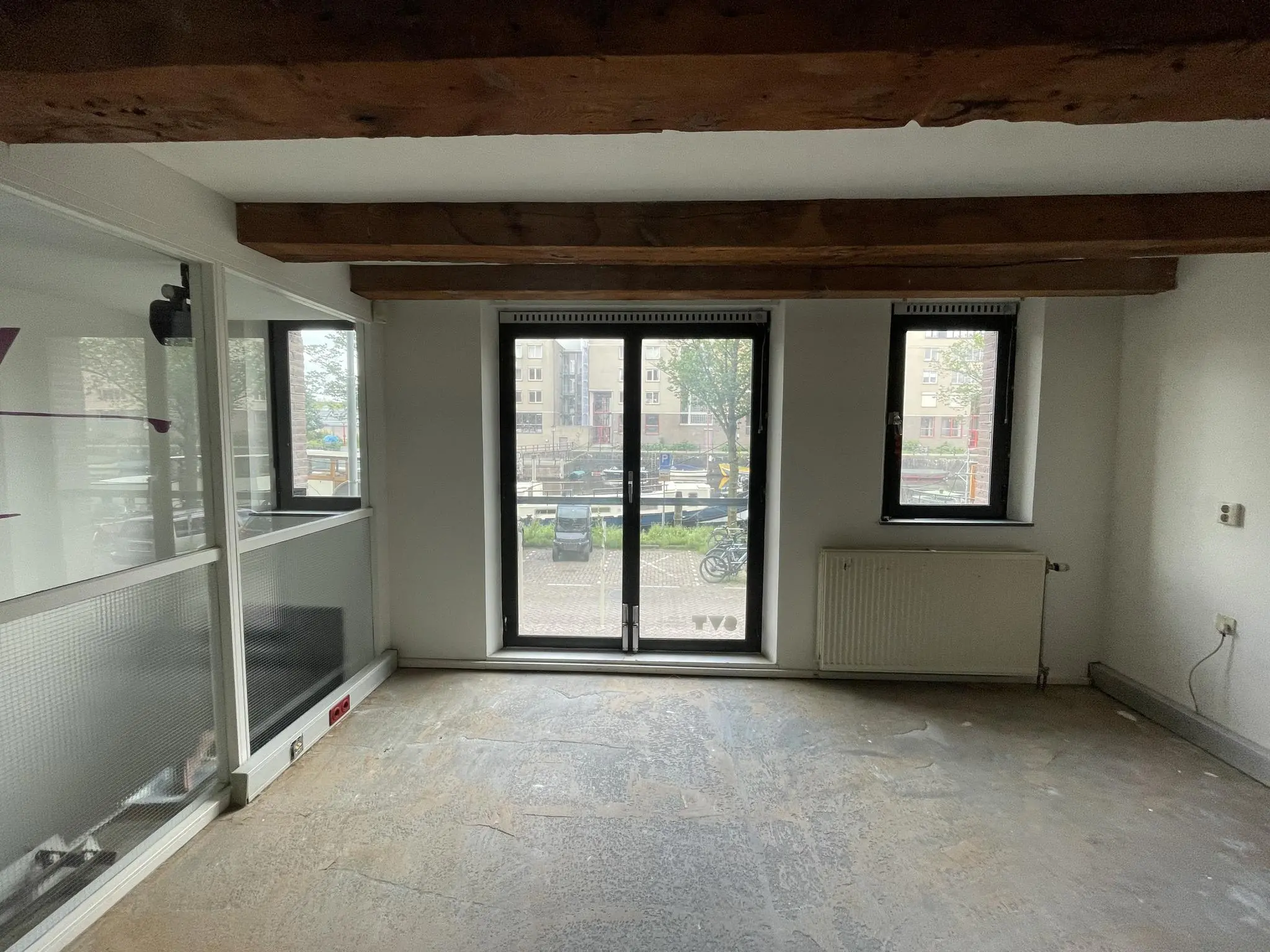 Leegstaand interieur van een ruimte aan het Entrepotdok met zicht op het buitenterrein en een gracht.