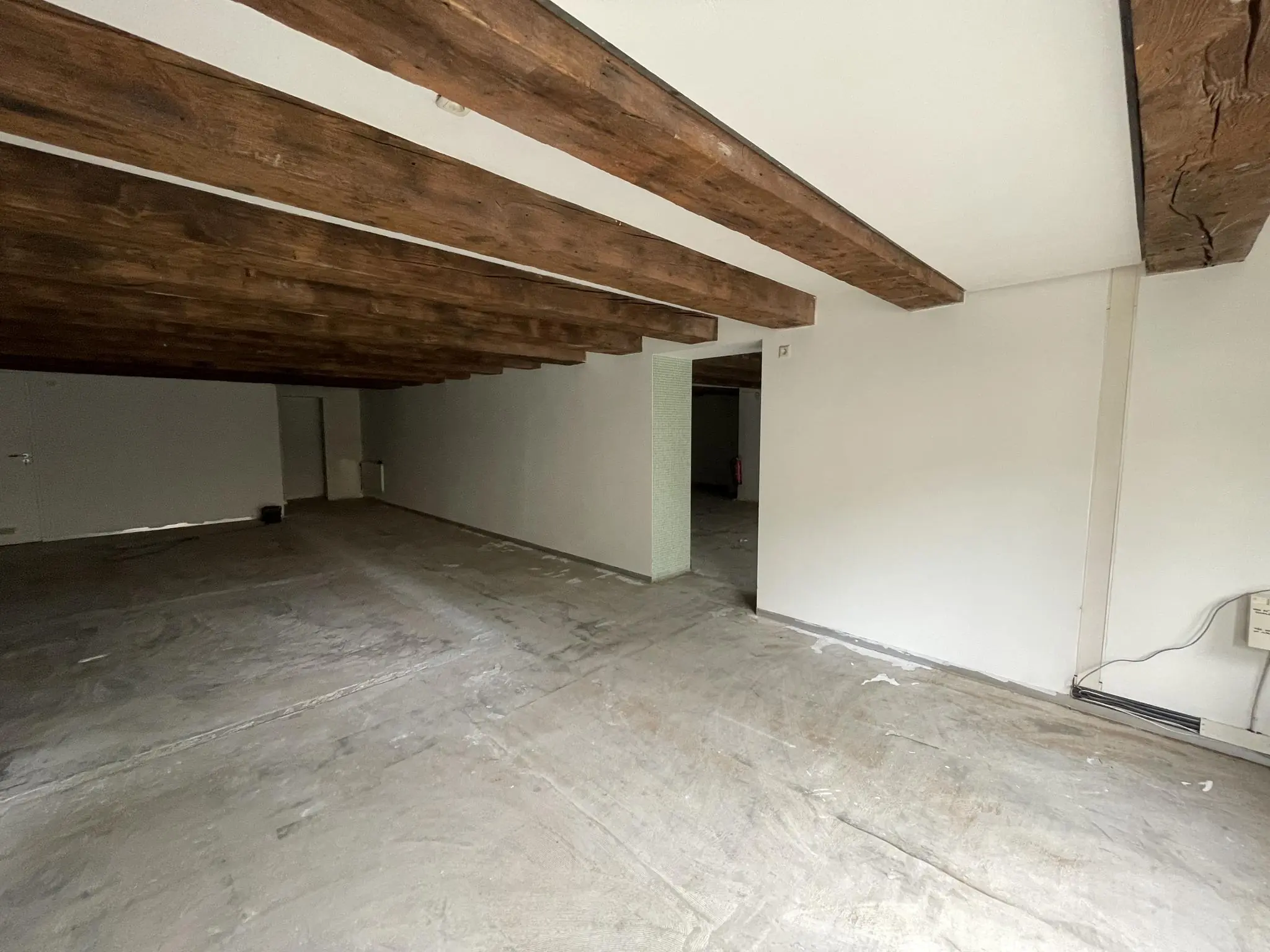 Lege ruimte in Entrepotdok met betonnen vloer, witte muren en zichtbare houten plafondbalken.