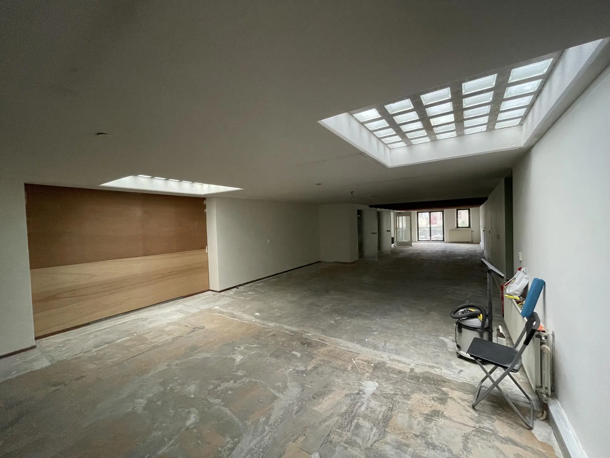 Leegstaand interieur van een ruim souterrain aan het Entrepotdok met betonnen vloer, daklichten en zicht op een glazen pui achterin.