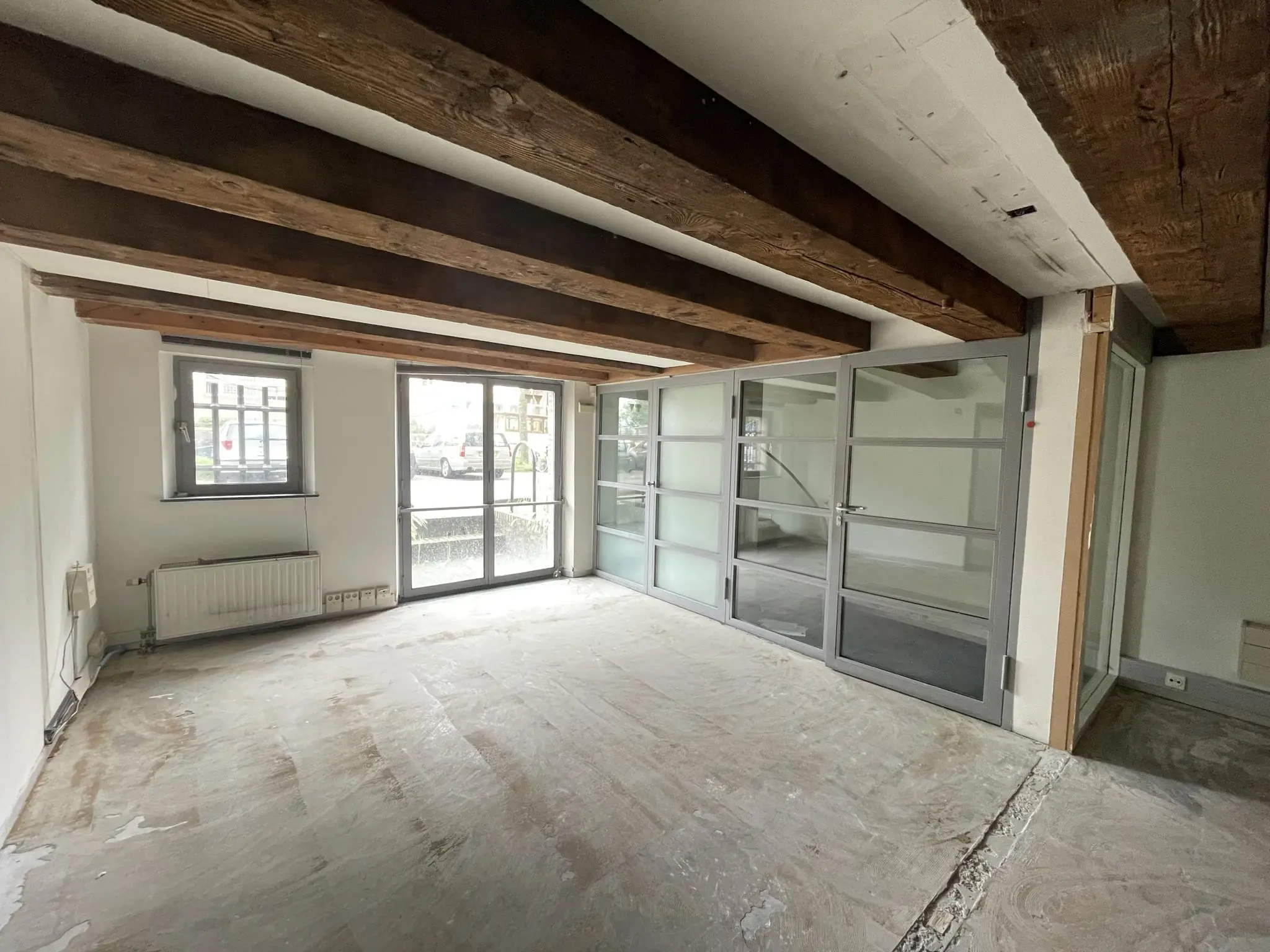 Leegstaand interieur van een ruimte aan het Entrepotdok met houten balkenplafond en glazen scheidingswanden.