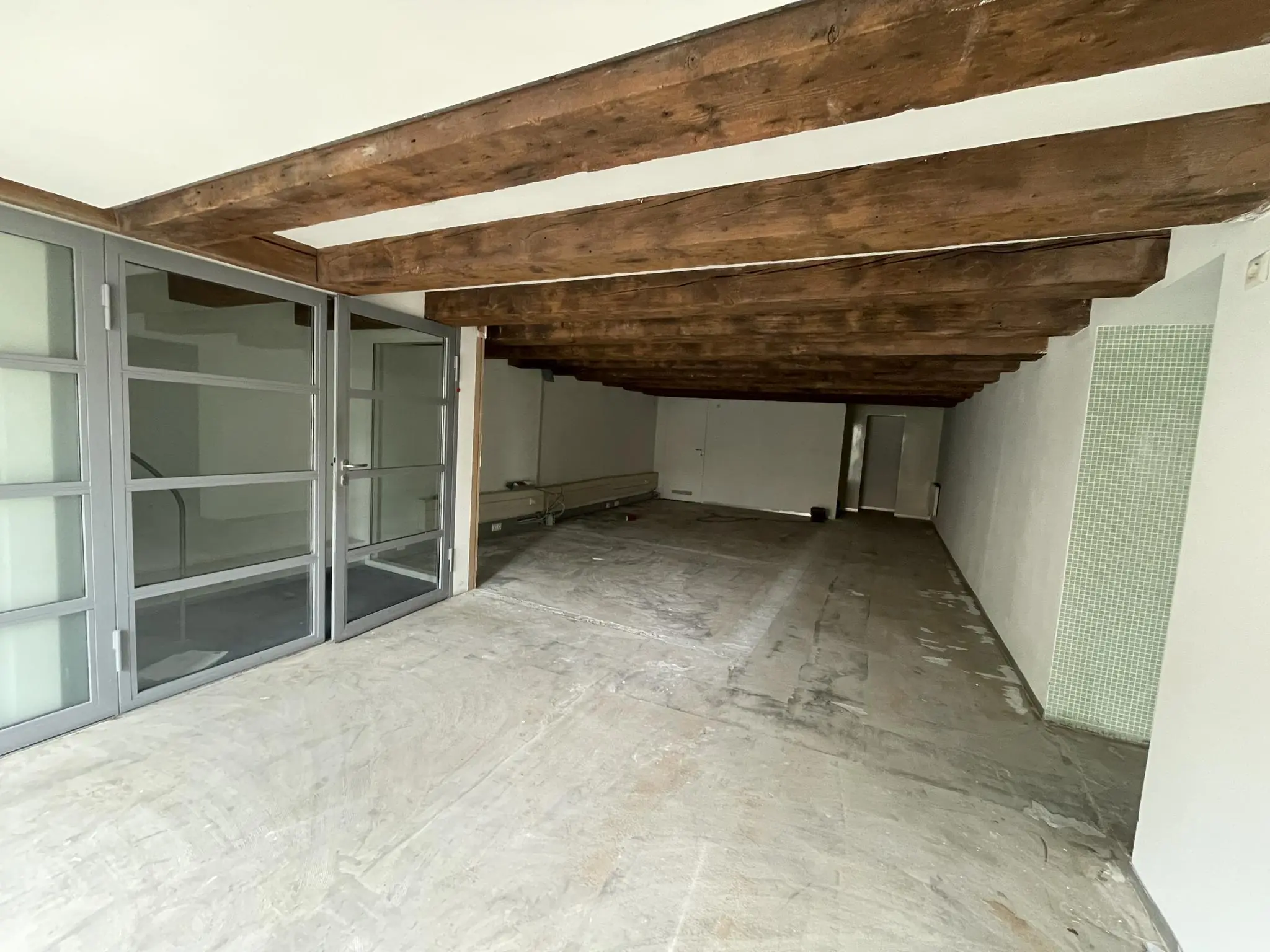 Leegstaand interieur van een ruimte aan het Entrepotdok met houten balkenplafond en glazen deuren.