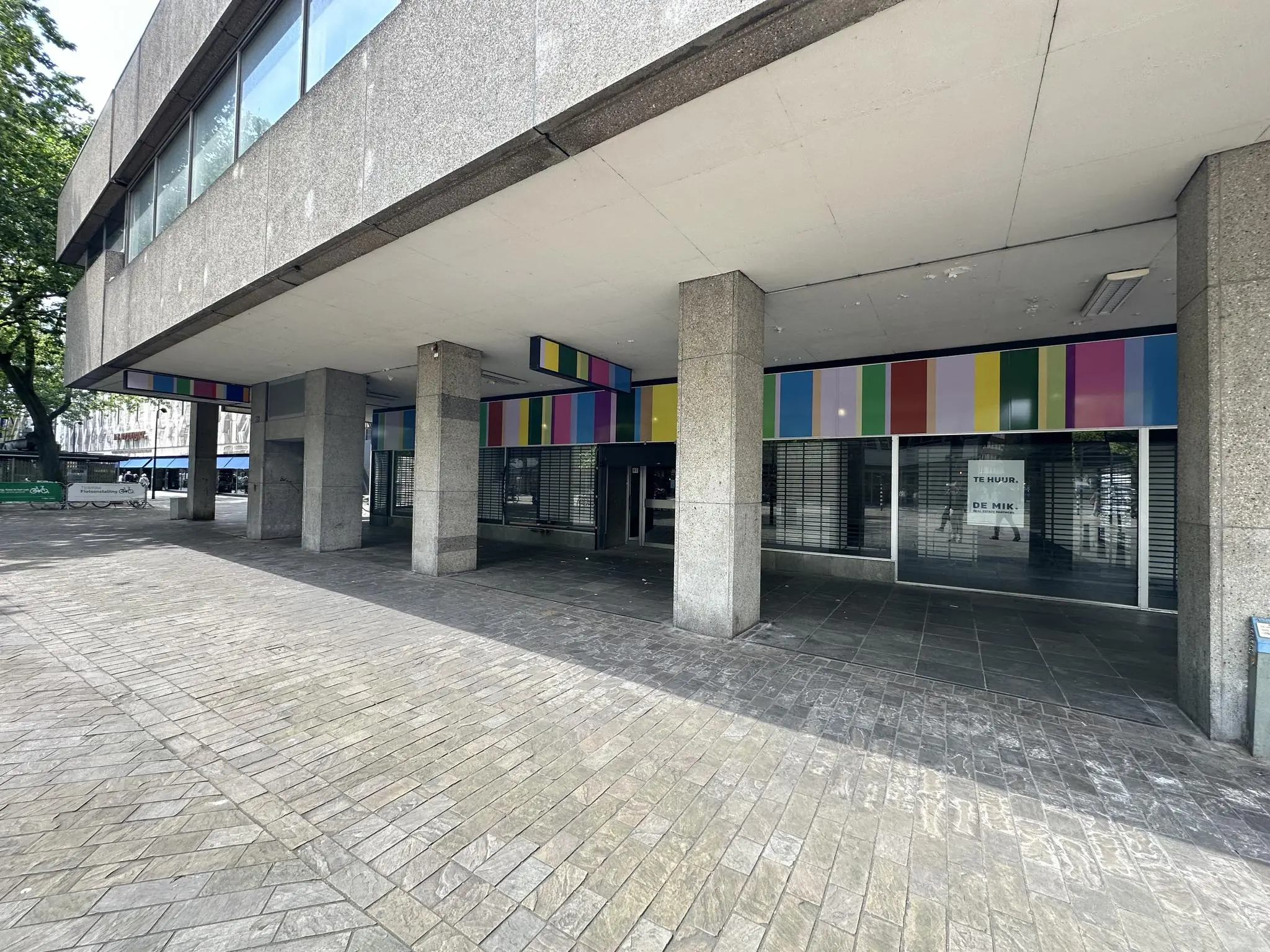 Leegstaand winkelpand aan de Coolsingel met gekleurde gevelpanelen en een 'Te huur' bord achter het raam.