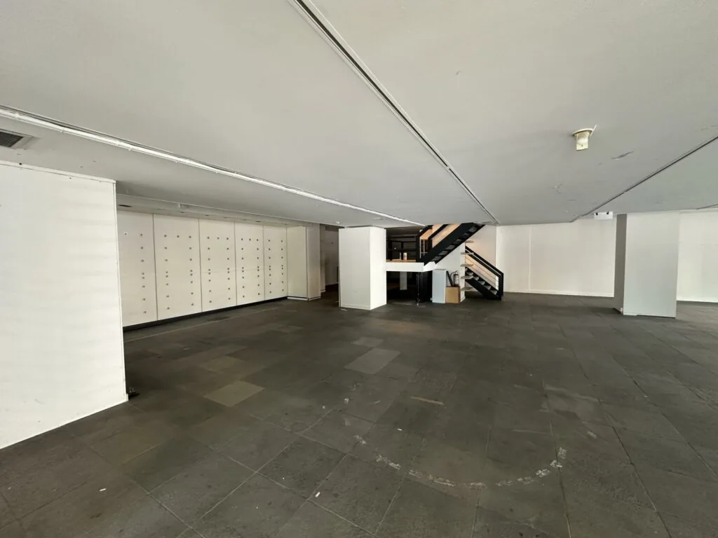 Leegstaand winkelpand aan de Coolsingel met donkere tegelvloer, witte muren en een zwarte trap naar de bovenverdieping.