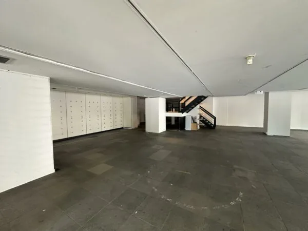 Leegstaand winkelpand aan de Coolsingel met donkere tegelvloer, witte muren en een zwarte trap naar de bovenverdieping.