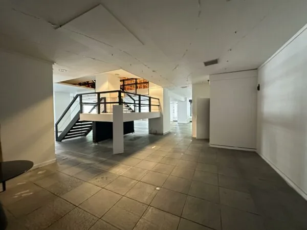 Leegstaand winkelpand aan de Coolsingel met grijze tegelvloer en een houten trap naar een entresol.