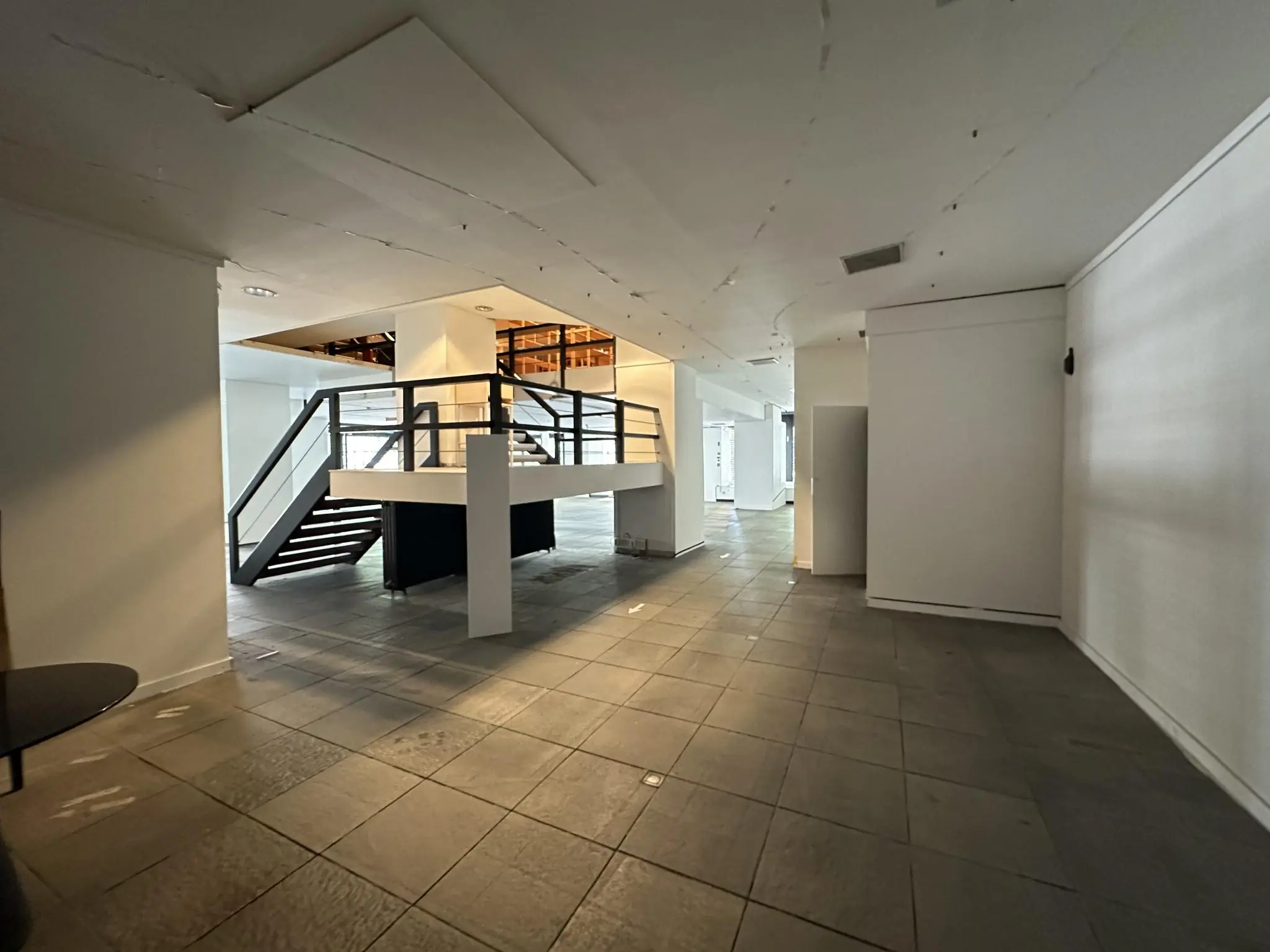 Leegstaand winkelpand aan de Coolsingel met grijze tegelvloer en een houten trap naar een entresol.