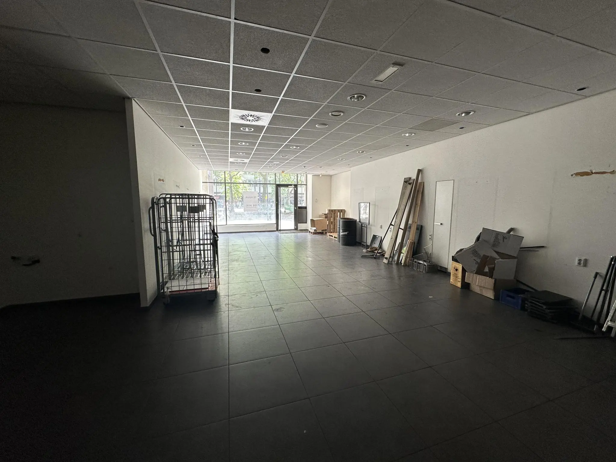 Leegstaand winkelpand aan de Coolsingel met bouwmaterialen en een metalen rolcontainer.
